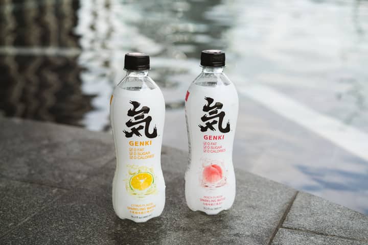 Close-up shot of Genki sparkling water bottles by the poolside, showcasing citrus and peach flavors.