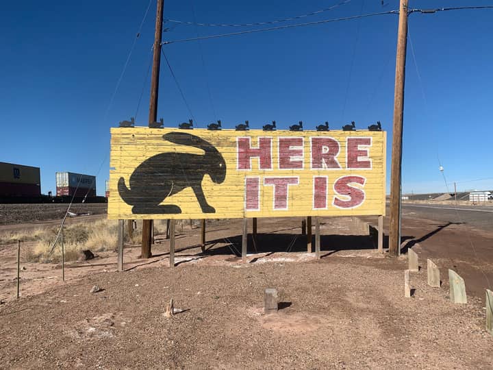 Historic Route 66 sign featuring a rabbit silhouette and the text 'HERE IT IS' under clear blue skies.