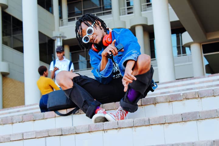 Stylish young adult sitting on urban stairs wearing headphones and sunglasses in Gaborone.
