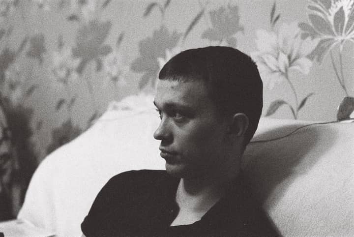 A man leans on a sofa, deep in thought, captured in striking black and white.