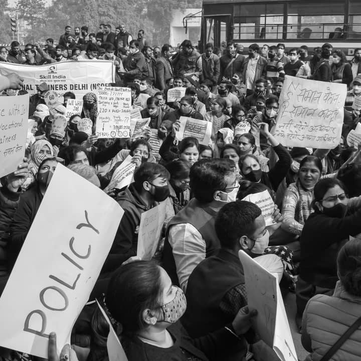 Black and white image of a crowded protest rally in Delhi advocating for policy reform.