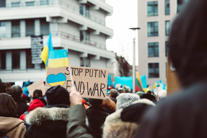 Peaceful protest in an urban setting featuring anti-war signage and Ukrainian flags.