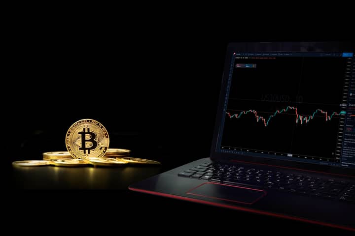 Golden bitcoin coins next to a laptop displaying a trading graph, symbolizing digital currency investment.
