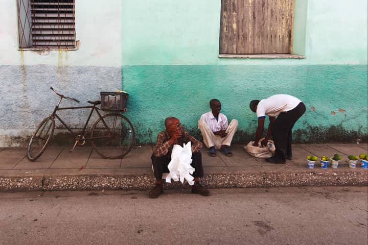 Men sitting on a sidewalk next to a bicycle, selling goods. Urban street scene.
