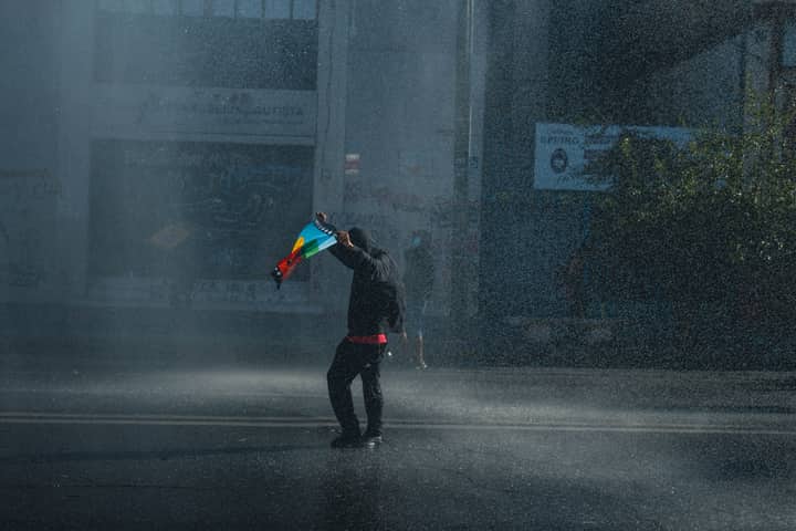 A lone protester holding a flag on a rainy street, symbolizing activism and resilience in Valparaíso, Chile.