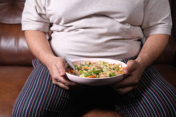 Individual sitting on a couch holding a bowl of vegetable salad, showcasing a healthy lifestyle.