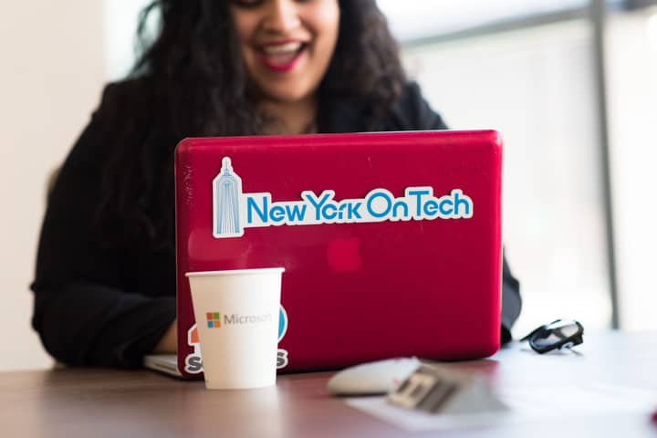 Young woman working remotely with a laptop in a modern indoor office setting, showcasing tech culture.