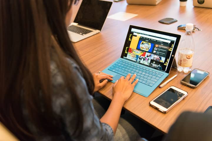 A woman working on a laptop at a wooden table with office devices around her.