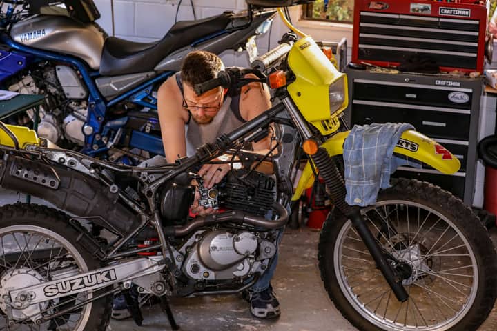 A mechanic repairs a Suzuki motorcycle engine inside a well-equipped garage.