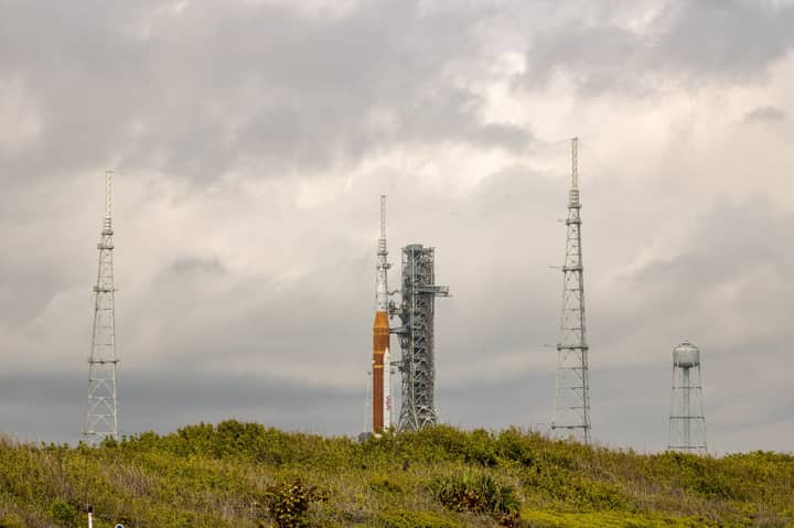 NASA rocket on launch pad surrounded by antennas against a cloudy sky.