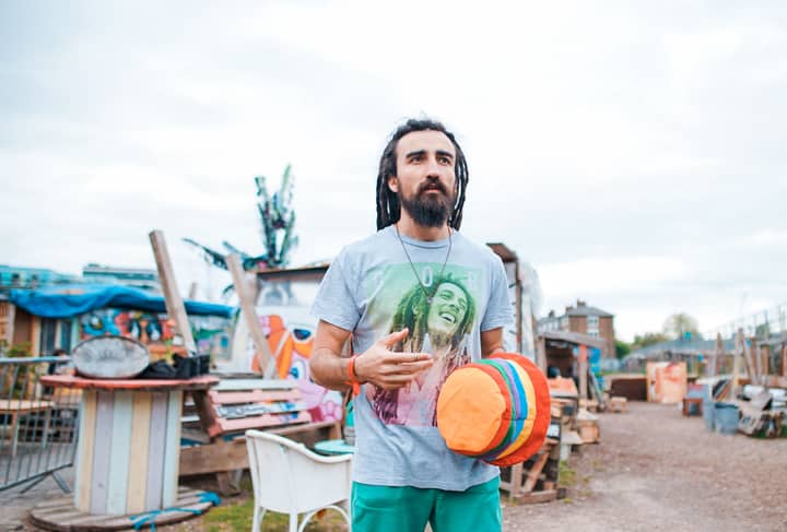 Man with dreadlocks holding a colorful hat in an outdoor creative space in London.