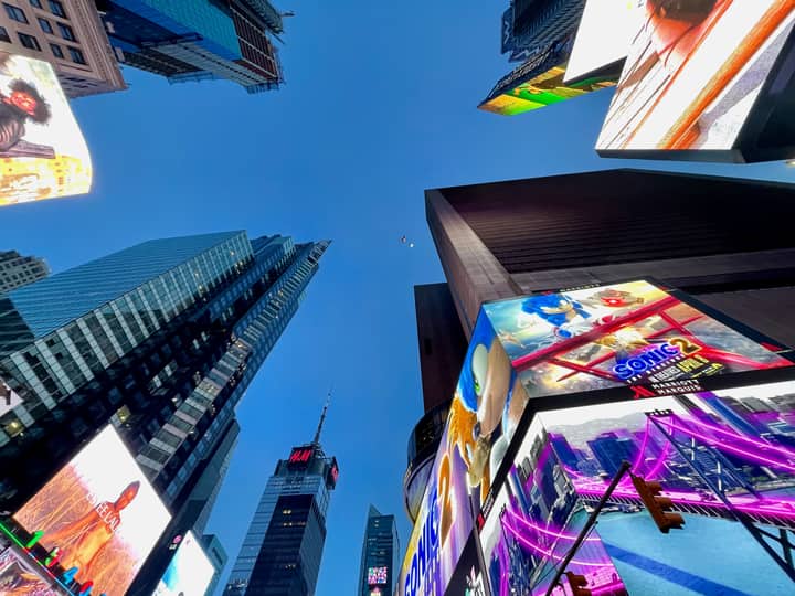 Low angle view of illuminated billboards and skyscrapers in Times Square, NYC at dusk.