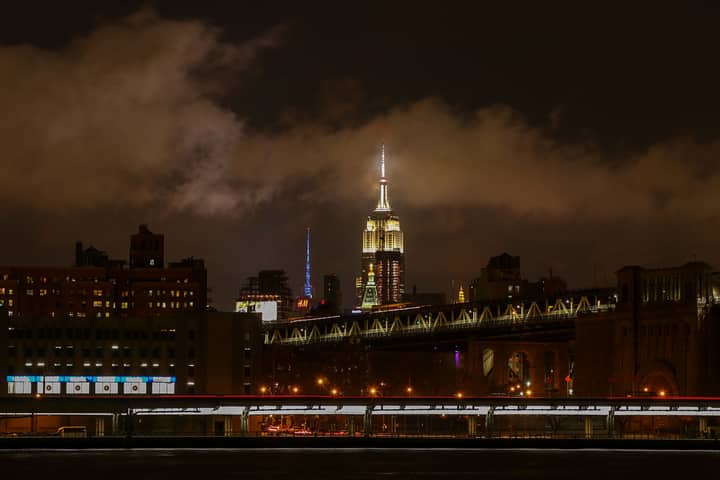 Captivating night view of the Empire State Building illuminated above the Brooklyn Bridge in New York City.