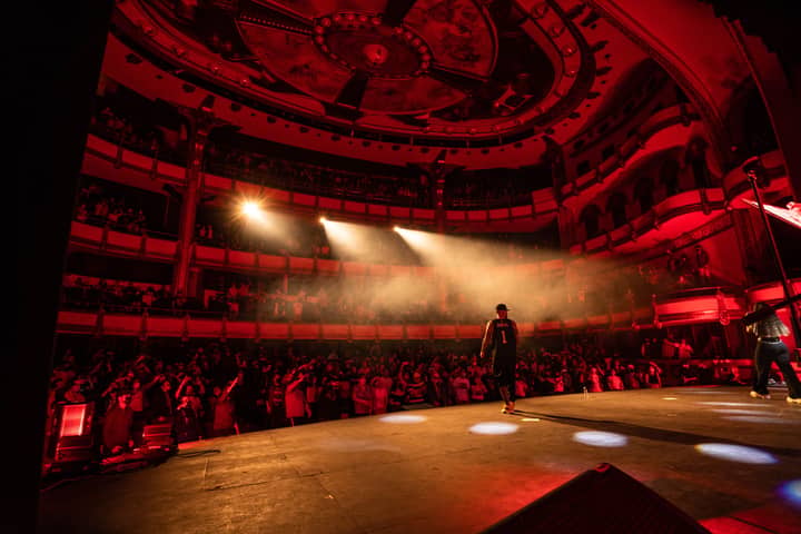 Live performance at Teatro de la Ciudad, Mexico City, with a dynamic audience and performers on a red-lit stage.