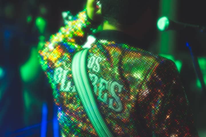 Back view of a musician in a sparkling jacket performing under colorful lights.