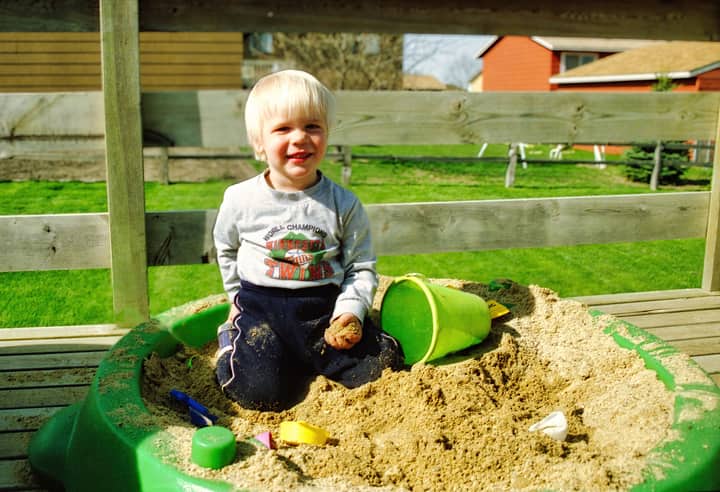 A cheerful toddler enjoying playtime in a backyard sandbox on a sunny day.