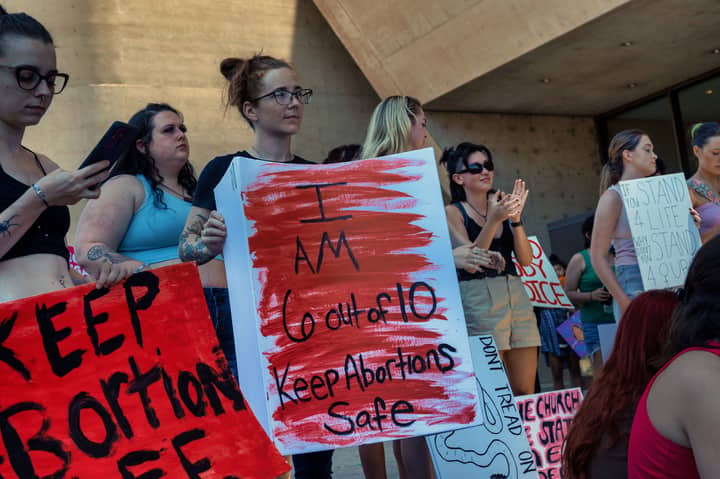 Women gather outdoors holding pro-abortion rights signs in an urban protest setting.