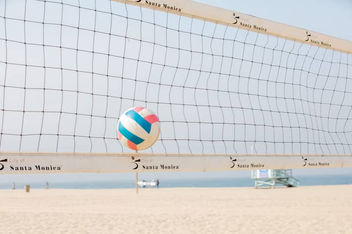 Colorful volleyball in mid-air at Santa Monica beach with net in foreground.