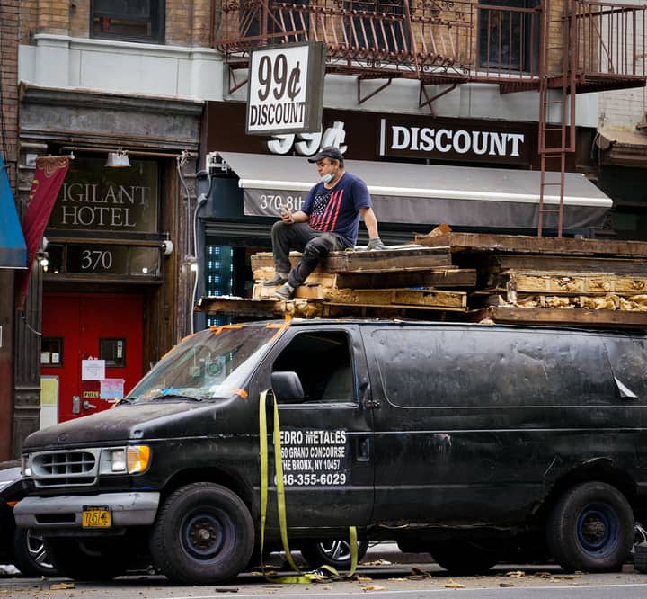 Man on top of loaded van in a bustling New York City streetscape with discount store signage.