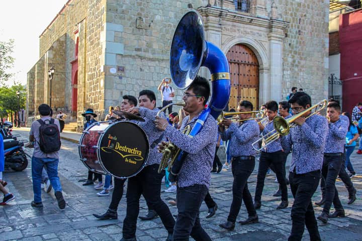 Vibrant brass band marches through historic Oaxaca street during a lively parade.