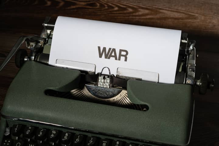 Close-up of an antique typewriter with the word 'WAR' typed on paper, on a wooden surface.