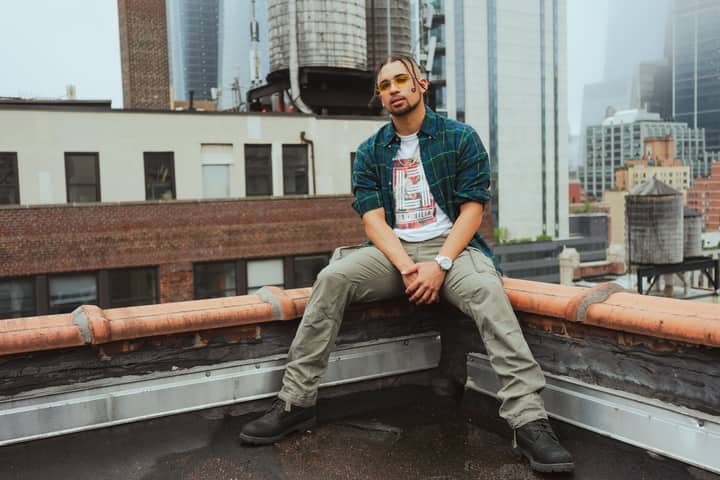 Stylish man posing on a New York City rooftop with skyline in the background.