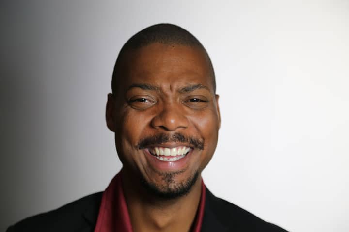 Studio portrait of a smiling bald man with facial hair, conveying happiness and positivity.