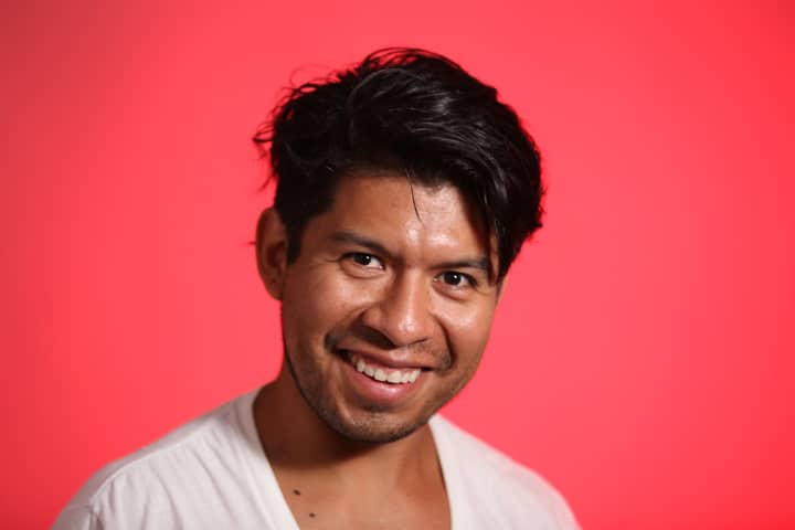 Vibrant studio portrait of a man smiling against a red backdrop.
