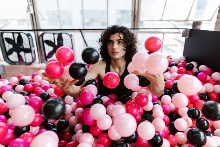 A young man plays joyfully in an indoor ball pit filled with vibrant balls.