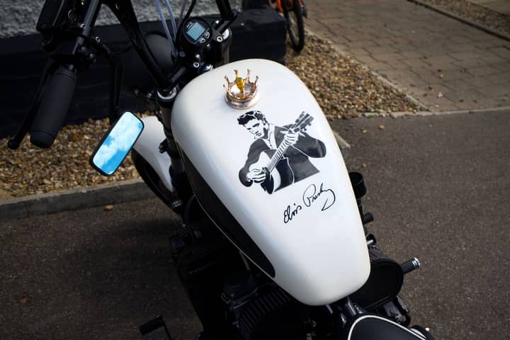 A vintage motorcycle featuring a guitar-playing musician design on its tank, parked outdoors.