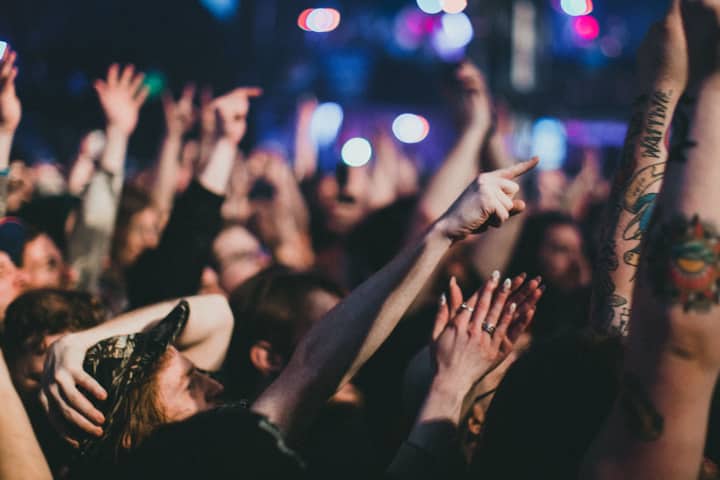 Vibrant concert crowd with raised hands and cheering under stage lights.