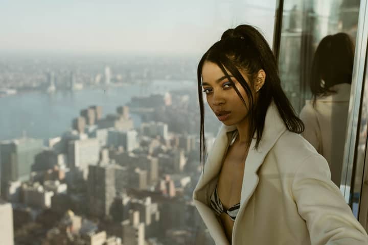 Stylish woman posing on an observation deck with a panoramic NYC skyline view.