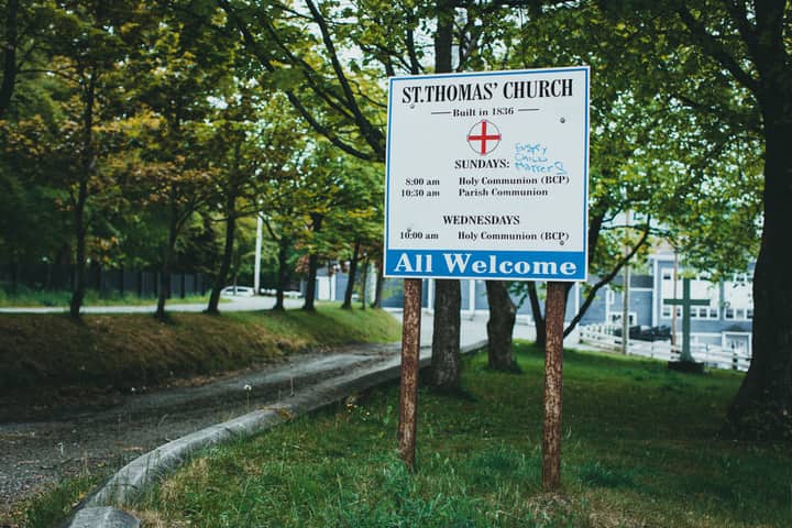 Welcome sign outside St. Thomas' Church surrounded by lush greenery and trees.
