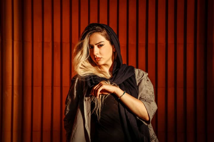 Blonde woman posing stylishly against a wood backdrop in a studio setting.