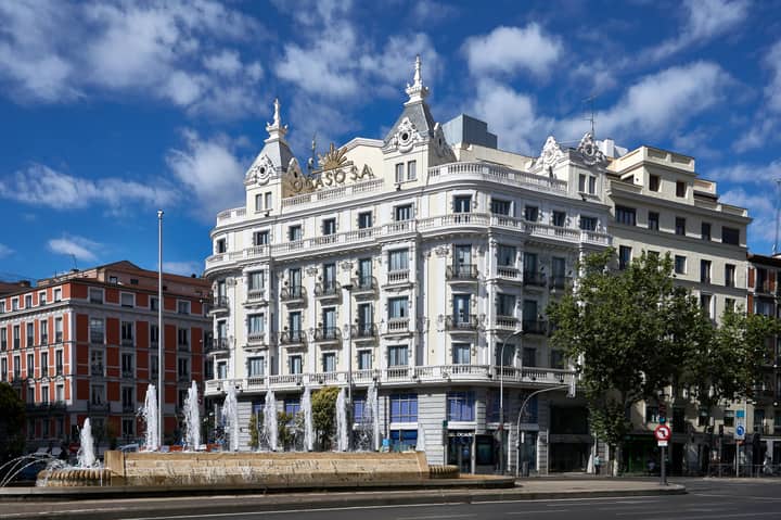 Charming architecture of a classic Madrid building with ornate facade and a lively fountain in daylight.