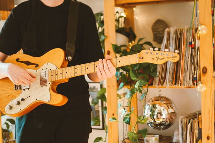 Close-up of a musician playing a Fender electric guitar indoors.