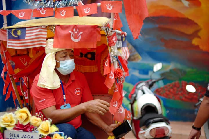 Capture of traditional rickshaw decorated with flags in Kota Bharu, Malaysia street scene.