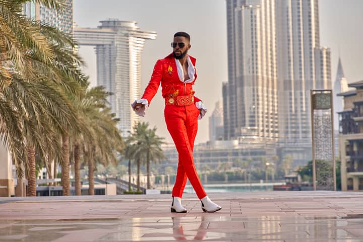Man in red fashion suit posing boldly against Dubai skyline, exuding confidence.