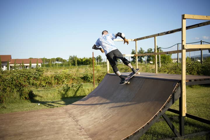Skateboarder executing a trick on a wooden outdoor skate ramp with lush greenery in the background.