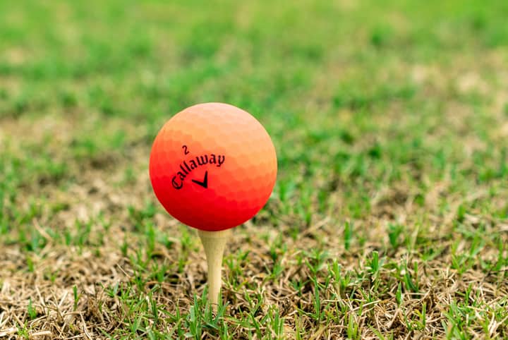 Close-up of an orange golf ball on freshly cut grass, ready for a tee-off.