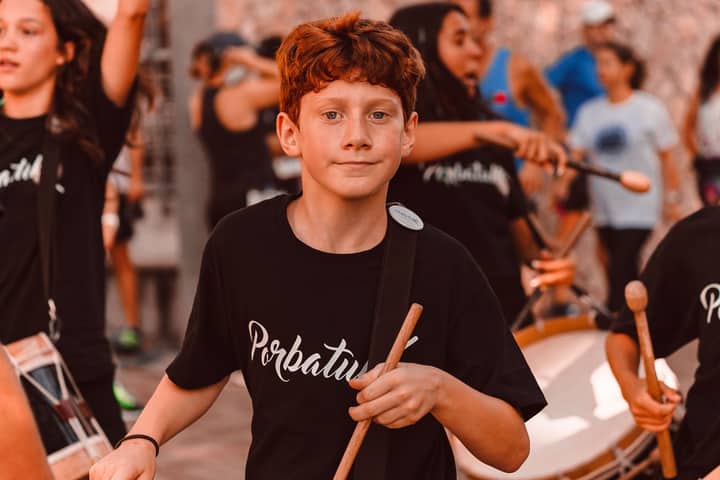 Teen drummer in a vibrant street performance with companion musicians.