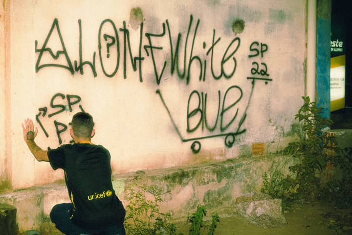 A young man sits in front of a graffiti-covered wall, embracing urban street art culture.