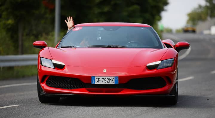 Front view of a red Ferrari driving outdoors, driver waving hand.