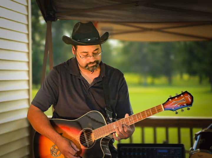 Musician with cowboy hat playing an acoustic guitar outside, enjoying the music.