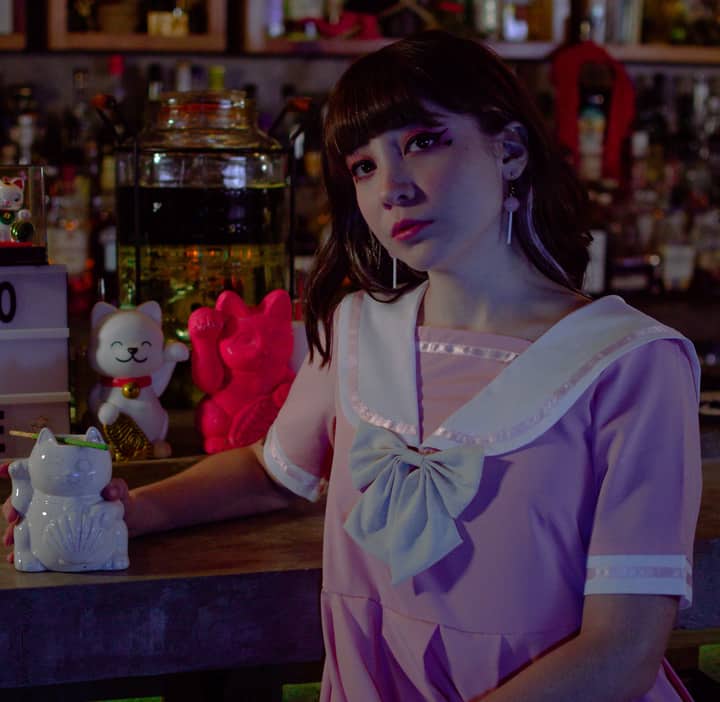 A young woman poses with cat figurines on a dimly lit bar counter in Mexico City.