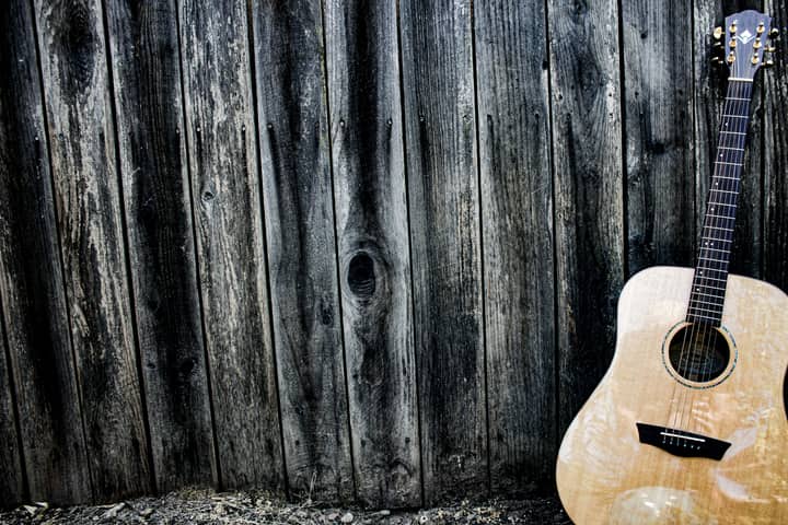 An acoustic guitar resting against a textured wooden wall, evoking a rustic musical charm.