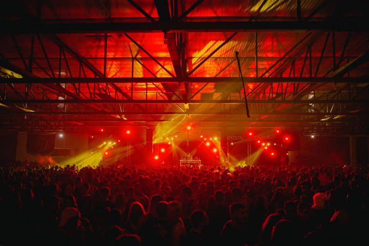 A lively indoor concert scene with a crowd under vibrant red and yellow lights.