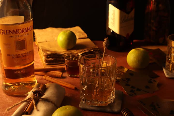 Warm still life featuring whisky, green apples, cinnamon sticks, and playing cards.