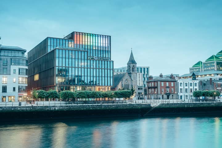 A vibrant cityscape featuring modern glass buildings along a tranquil riverfront in a bustling urban environment.