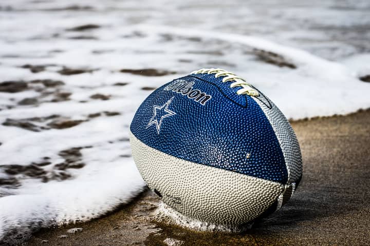 Close-up of a blue football resting on wet sand by the ocean shore.